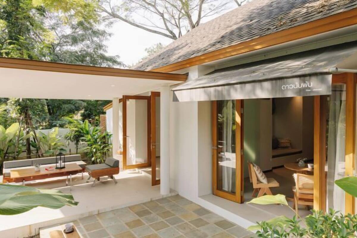 A modern outdoor patio area with a wooden bench and a table, surrounded by lush greenery.