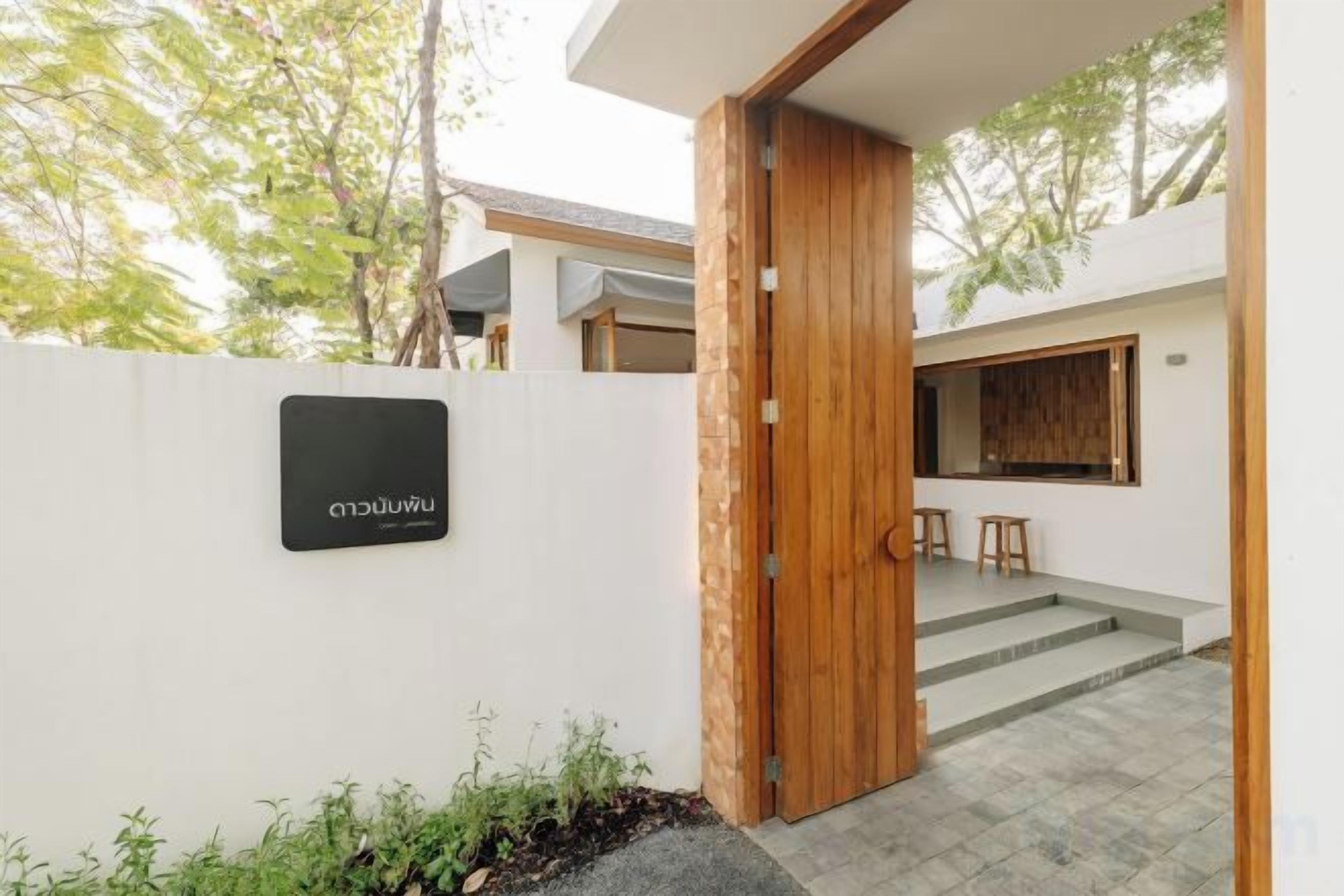 A modern entrance with a wooden door, a white wall with a sign, and a staircase leading to a covered area.