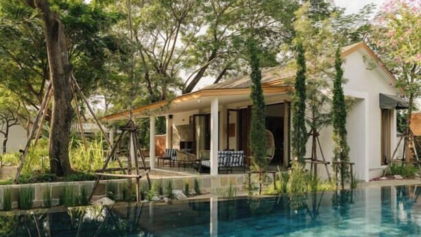 Un espace aménagé au bord de la piscine, doté d’un coin salon couvert, entouré d’arbres et donnant sur une piscine aux eaux cristallines.