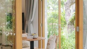 Une pièce avec une table et des chaises en bois, une fenêtre avec des rideaux et une vue sur la verdure à l’extérieur.