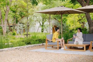 A garden setting with outdoor seating, including a sofa and a chair, under a large umbrella. - ดาวนับพัน Baan Phandao (Mae Rim)