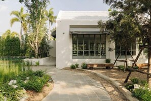 A modern house with a paved pathway leading to the entrance, surrounded by greenery and a small pond. - ดาวนับพัน Baan Phandao (Mae Rim)