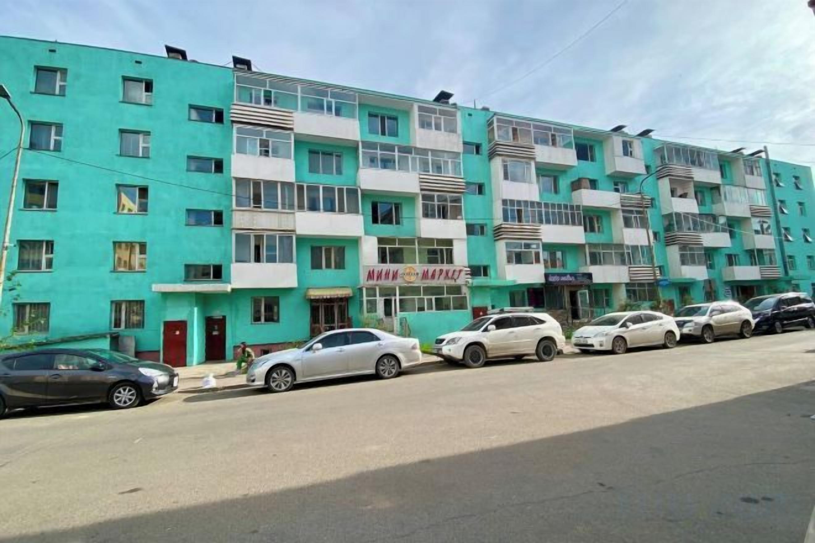 A multi-story residential building with several parked cars in front.