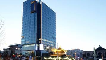 A modern high-rise building with a glass facade, a traditional Asian-style pavilion with golden decorations, and a clear sky.