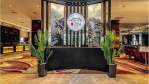 Un espace d’accueil au design moderne, comprenant un comptoir noir, deux plantes en pot et un logo avec le mot « ZEN » affiché sur le mur.