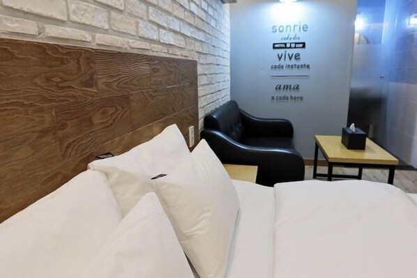 A hotel room with a brick-patterned headboard, a black leather chair, a small wooden table, and a wall-mounted sign with text. - sweetdream (Jinju)