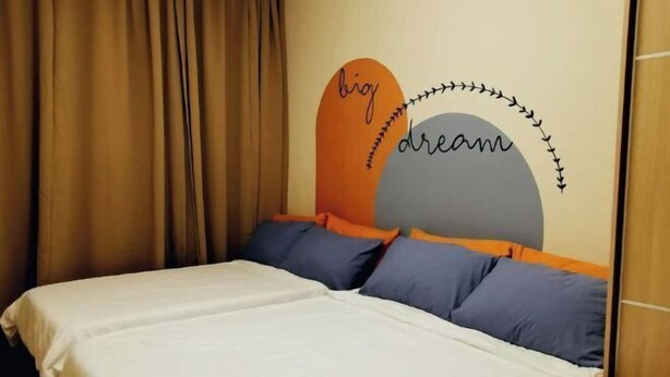 Cama com roupa de cama branca, almofadas azuis e parede com um desenho circular e texto.