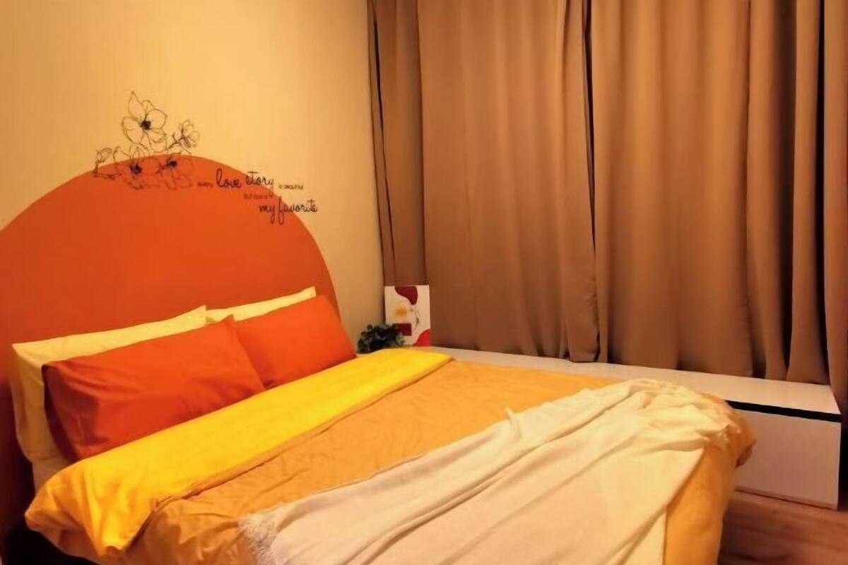 Un lit avec une literie aux couleurs orange et blanche, une tête de lit ornée d’un motif floral et un mur décoré d’une citation.