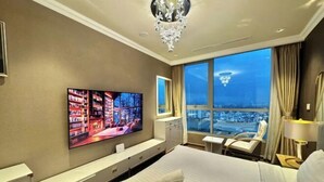 A hotel room with a large bed, a TV mounted on the wall, a view of the city through the window, and a chandelier. - VINHOMES CENTRAL PARK LUXURY APARTMENT (Ho Chi Minh City)