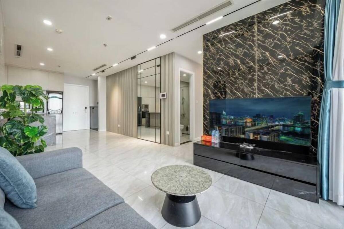 Een moderne hotel lobby met een bank, een ronde tafel, een groot televisiescherm en uitzicht op de stad.