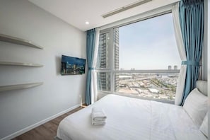 A hotel room with a large window, a bed, a painting on the wall, and a view of the cityscape. - VINHOMES CENTRAL PARK LUXURY APARTMENT (Ho Chi Minh City)
