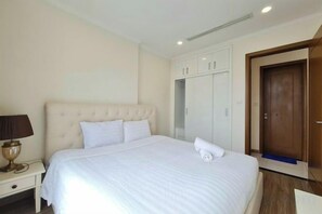 Une chambre d’hôtel avec un grand lit, une armoire, une table de chevet avec une lampe et une porte.