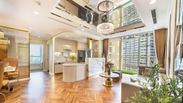 A spacious living area with a herringbone wood floor, a central island, and a large window offering a view of high-rise buildings. - VINHOMES CENTRAL PARK LUXURY APARTMENT (Ho Chi Minh City)