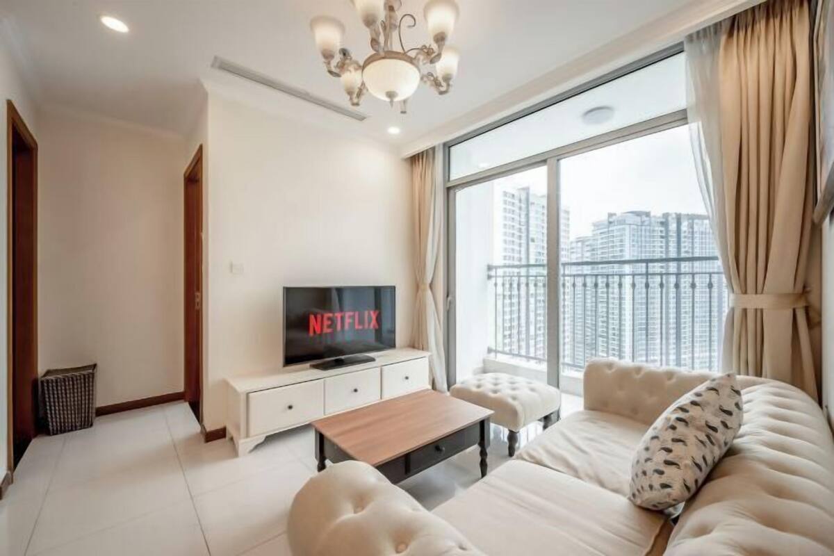 Een moderne woonkamer met een televisie waarop 'NETFLIX' staat, een bank, een salontafel en een groot raam met uitzicht op de stad.