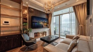 A modern living room with a sofa, a TV, a fireplace, and a balcony with a view. - VINHOMES CENTRAL PARK LUXURY APARTMENT (Ho Chi Minh City)