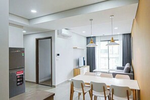 Une chambre d’hôtel moderne dotée d’un coin repas, d’une kitchenette et d’une grande fenêtre avec des rideaux.