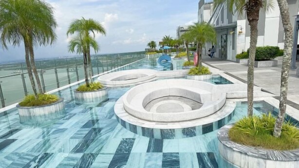 Een modern buitenzwembad met ronde waterattracties en palmbomen, omgeven door een glazen balustrade met uitzicht op de oceaan.