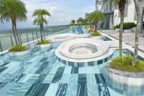 Zona de piscina exterior moderna amb elements aquàtics circulars i palmeres, emmarcada per una barana de vidre amb vistes a l'oceà.