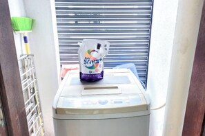 A room with a window, a metal shutter, a laundry machine, and a bottle of laundry detergent. - Damas Mont Kiara by Scape Stay (Kuala Lumpur)