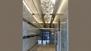 A modern hallway with marble walls, a chandelier, and a glass elevator. - Damas Mont Kiara by Scape Stay (Kuala Lumpur)