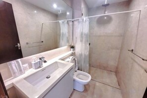Un baño moderno con un espejo grande, un lavamanos, un inodoro y una zona de ducha.