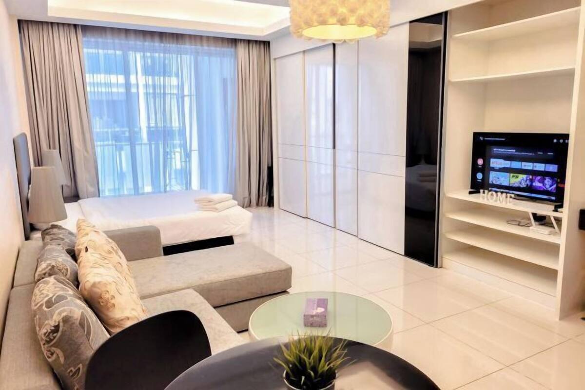 A modern hotel room with a bed, sofa, TV, and a glass coffee table.