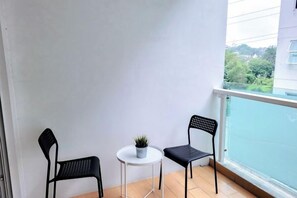 A balcony with two chairs and a small table, a potted plant, and a view of greenery. - Damas Mont Kiara by Scape Stay (Kuala Lumpur)