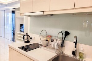 Una cocina moderna con una placa de inducción negra, un lavamanos de acero inoxidable y un horno empotrado. Hay una encimera blanca con una tetera y una cafetera.