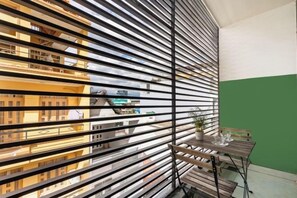 A room with a large window featuring horizontal blinds, a small table with a glass, and a view of buildings outside. - Gemini Saigon Center - New & Quiet Near Bui Vien Walking Street (Ho Chi Minh City)
