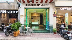 La entrada al Gemini Saigon Center con un diseño moderno, que presenta una puerta de cristal y un pequeño área de asientos al aire libre con sillas y plantas en macetas.