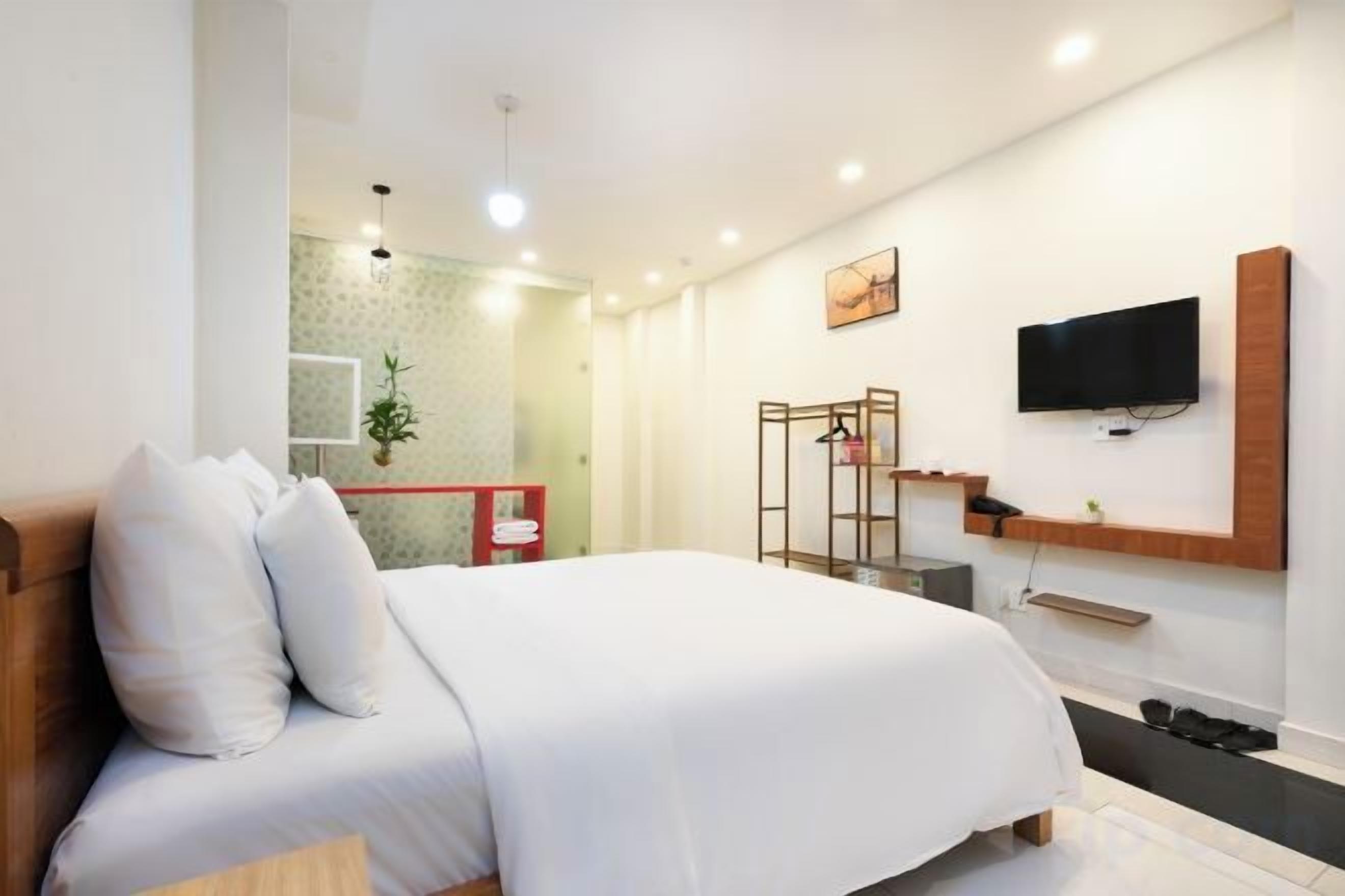 Une chambre d’hôtel avec un lit, un téléviseur fixé au mur et un petit coin salon avec un banc.