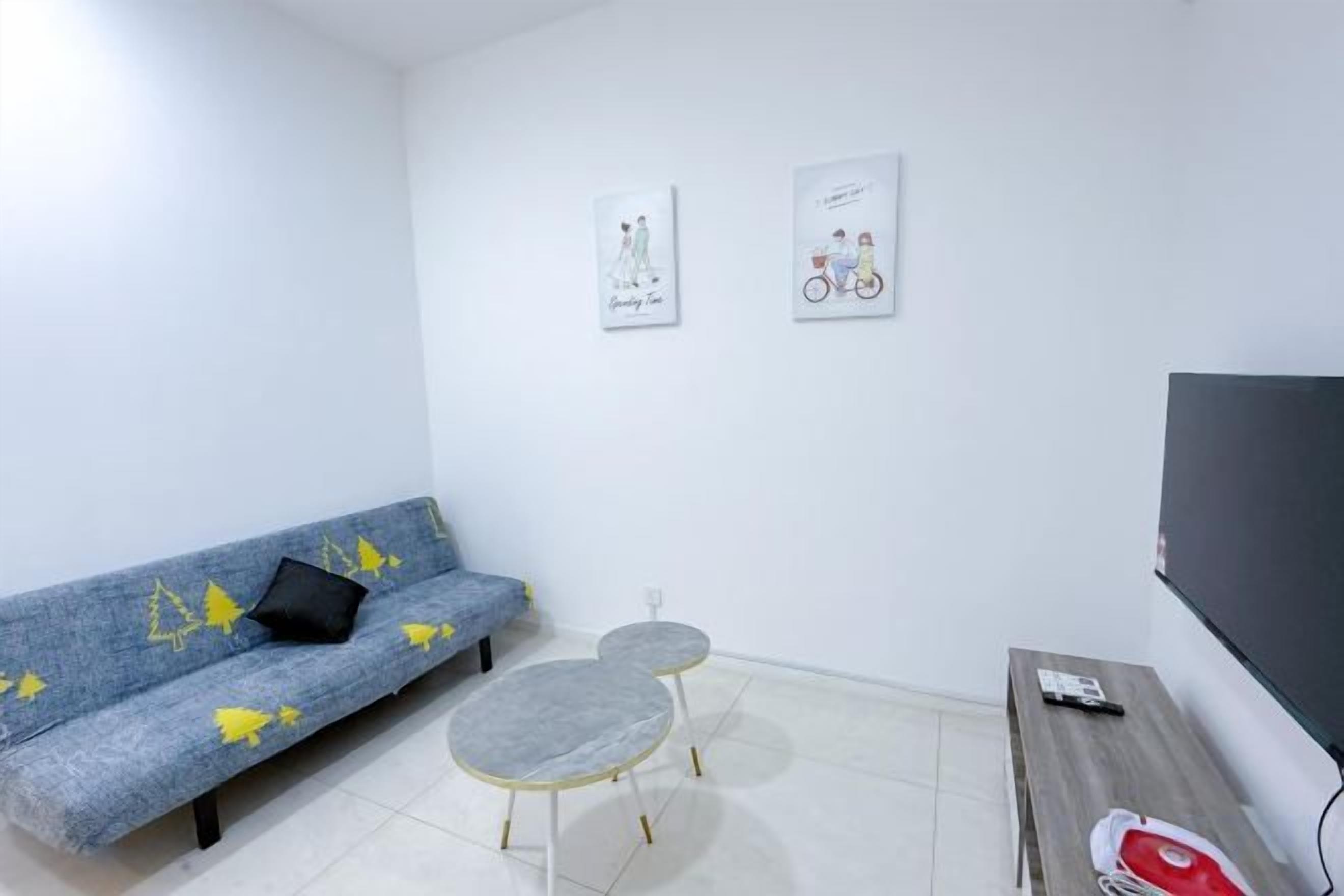 A room with a sofa, two small tables, a flat-screen TV, and artwork on the wall.