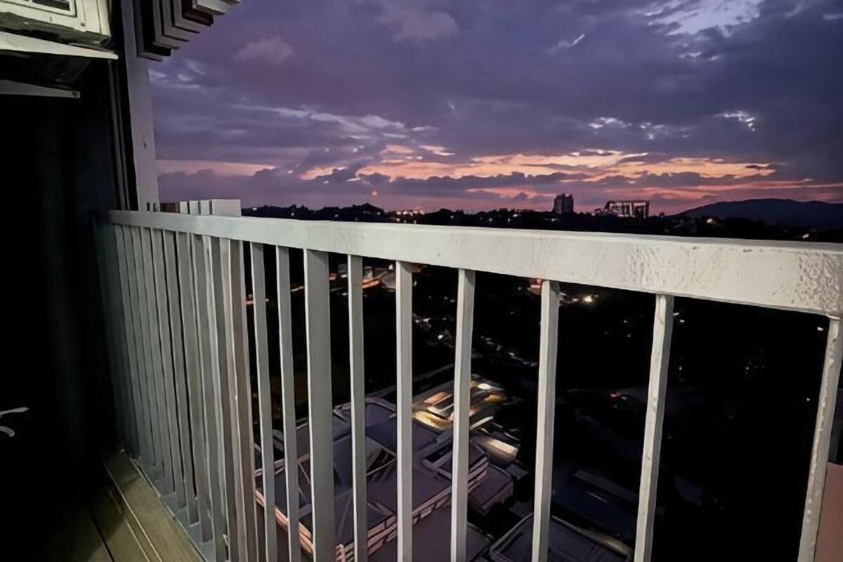 A balcony with a railing, overlooking a cityscape at dusk with buildings and lights.
