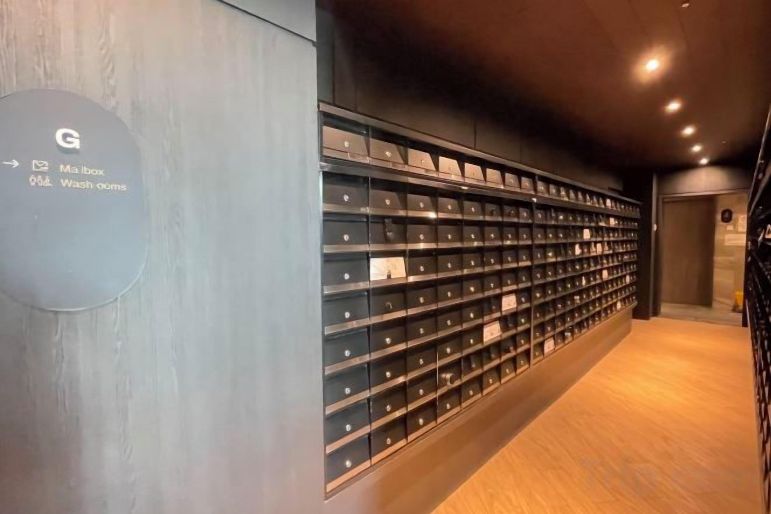 A hallway with a wall-mounted display of neatly arranged items, a sign indicating amenities, and a wooden floor.