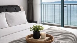 Une chambre à coucher avec un lit, une plante en pot, une bougie et une vue sur la mer depuis un balcon.