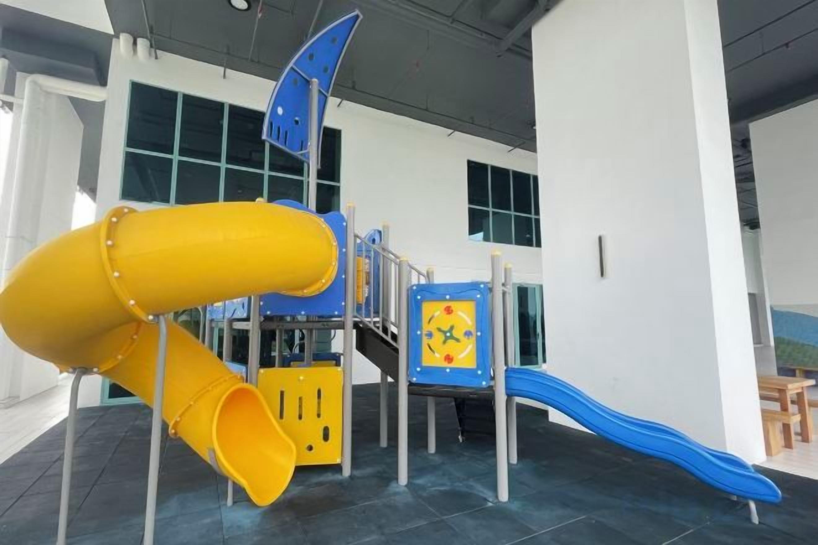 Un área de juegos interior con un tobogán amarillo, un tobogán azul y una estructura de juego.