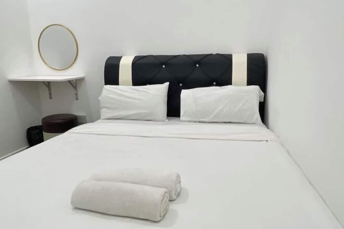 A neatly made bed with white linens, a black tufted headboard, and a round mirror on a small white shelf.