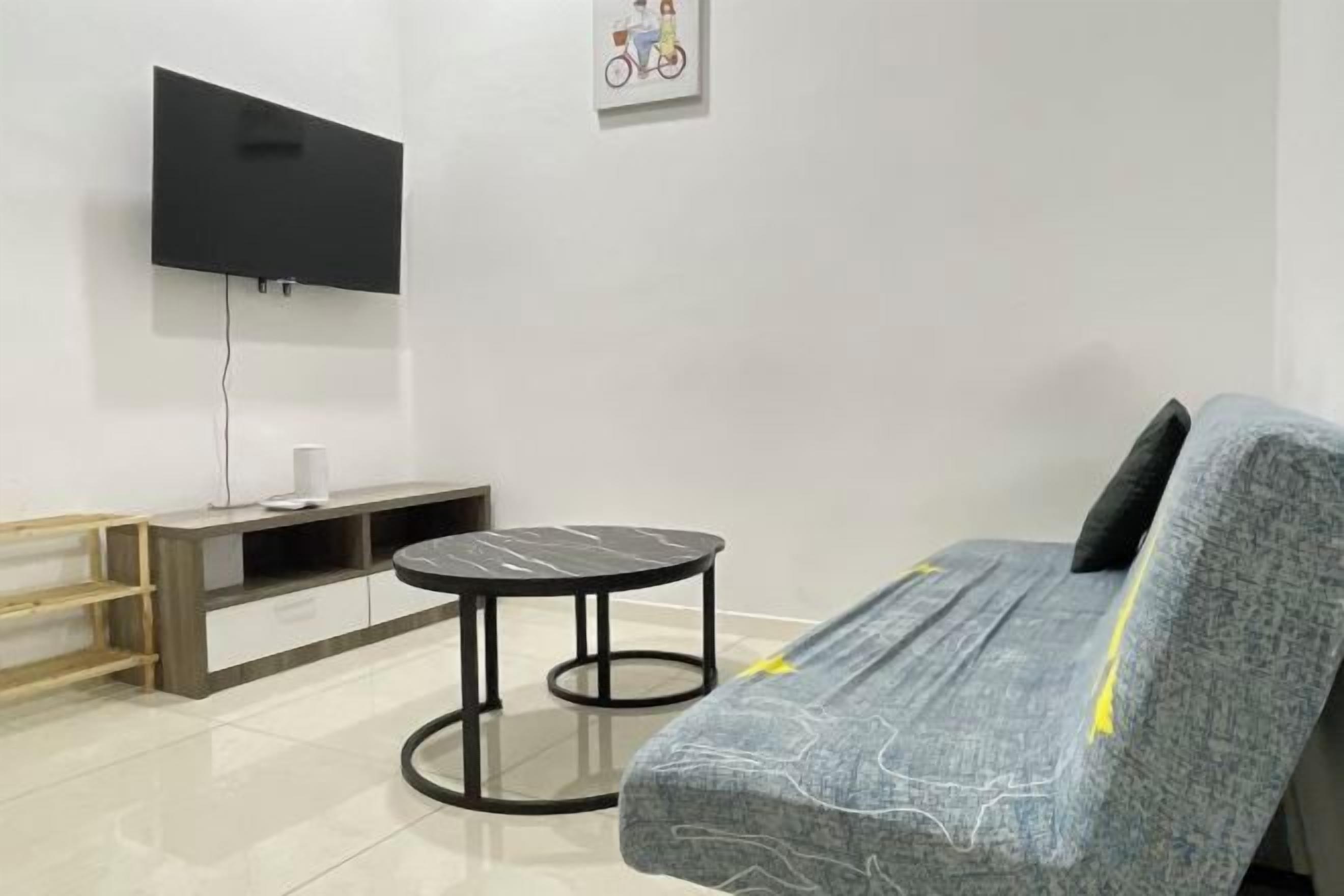 A modern living room with a sofa, a small round table, and a flat-screen TV mounted on the wall.
