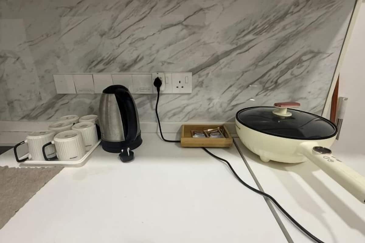 A kitchen with a marble backsplash, a kettle, a rice cooker, and a tray of white mugs.