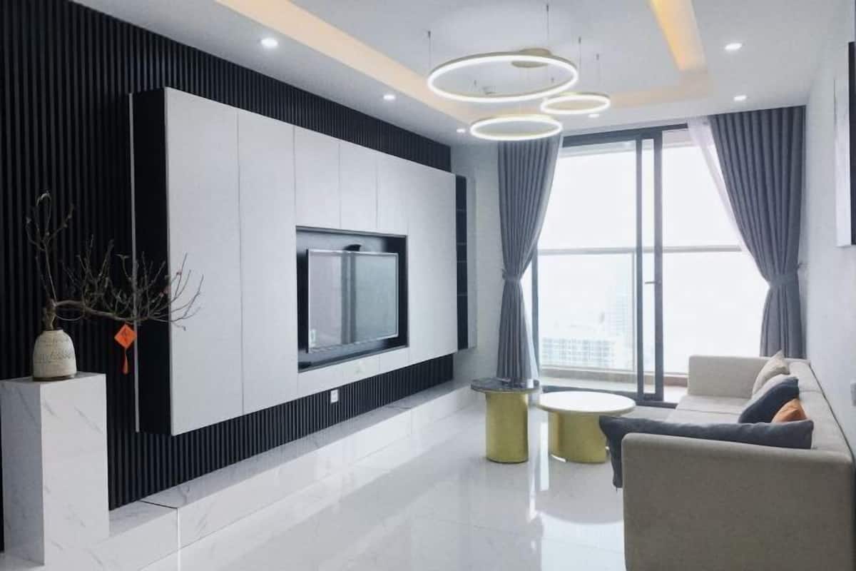 A modern living room with a flat-screen TV mounted on a white wall, a round coffee table, a sofa, and a large window with curtains.