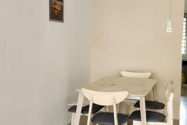 Un área de comedor con una mesa, sillas, un interruptor de luz en la pared y un cuadro enmarcado.