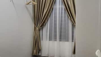 A corner room with a bed, a hanging clothes rack, and a window with curtains.