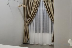 A corner room with a bed, a hanging clothes rack, and a window with curtains. - LestariHome2, KLIA Sepang (Sepang)