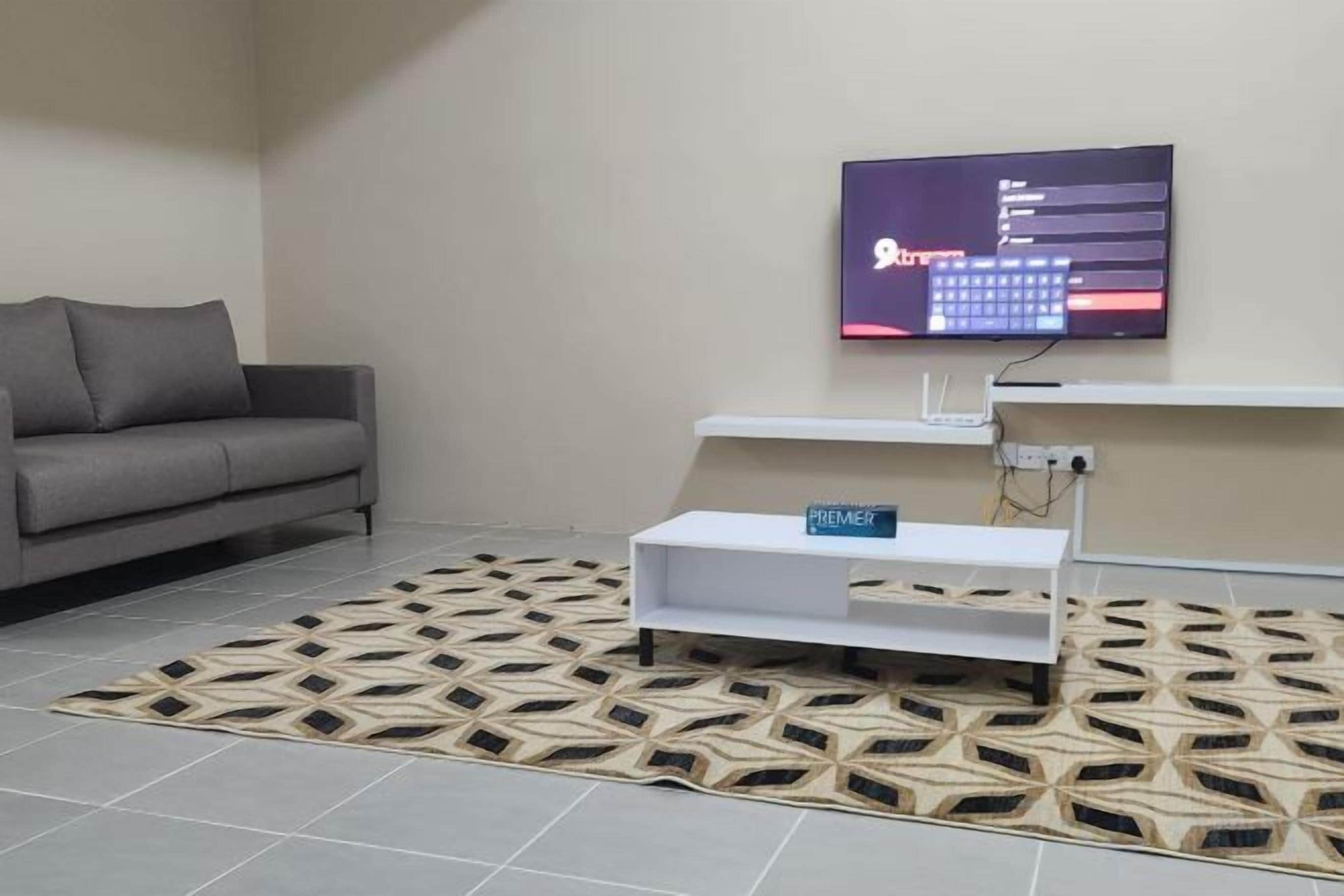 A modern living room with a grey sofa, a flat-screen TV mounted on the wall, a white console table, and a patterned rug.