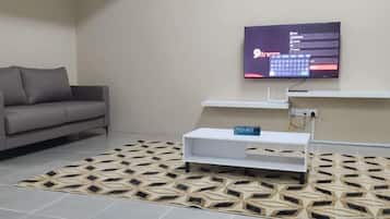 A modern living room with a grey sofa, a flat-screen TV mounted on the wall, a white console table, and a patterned rug.