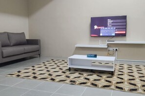 A modern living room with a grey sofa, a flat-screen TV mounted on the wall, a white console table, and a patterned rug. - LestariHome2, KLIA Sepang (Sepang)