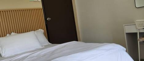 A hotel room with a bed, a door, and a desk.
