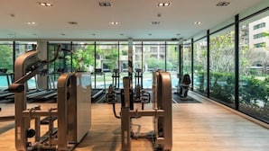 A modern gym with cardio equipment and large windows offering views of greenery and buildings.