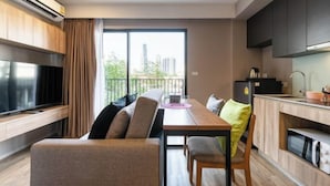 A modern apartment with a dining area, kitchenette, and a large window offering a city view.