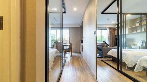 A modern hotel room with a wooden floor, a glass partition, and a bed with a white cover.